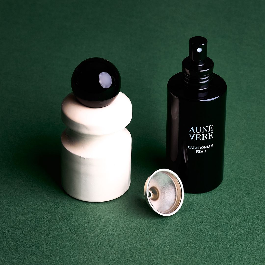 Caledonian Pear ceramic vessel with its 100 ml bottle and a silver funnel, assembled on green paper.
