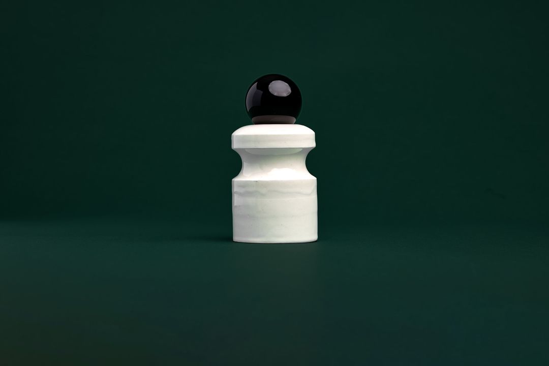 Caledonian Pear ceramic vessel, a faceted dark glazed base holding a clear glass orb, on mossy green paper.