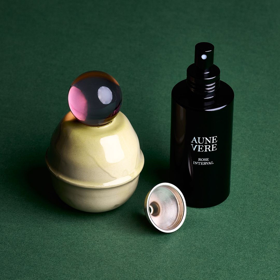 Rose Interval ceramic vessel with its 100 ml bottle and a silver funnel, assembled on green paper.