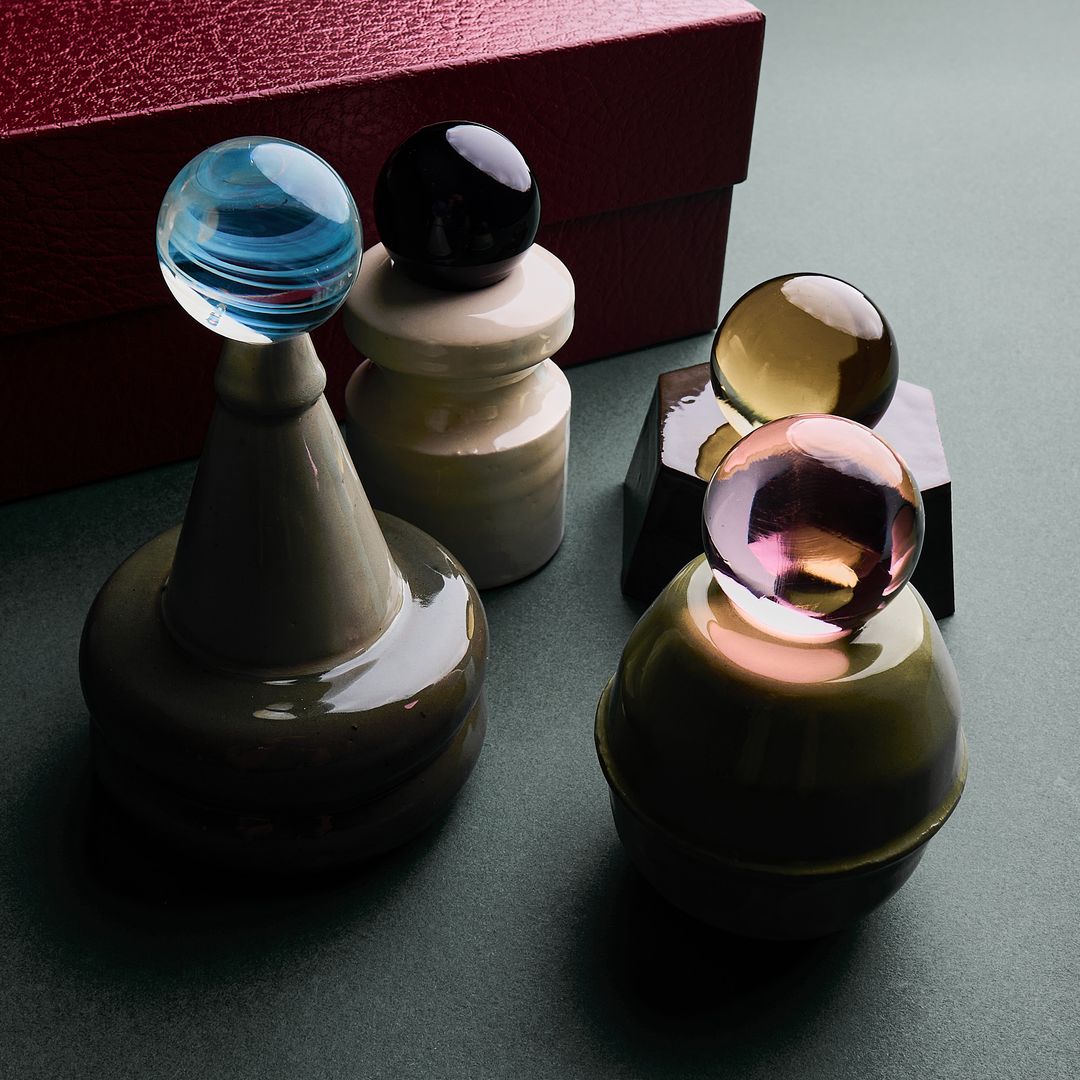 The four Collection 001 ceramic vessels grouped before a burgundy box, each holding its glass orb.